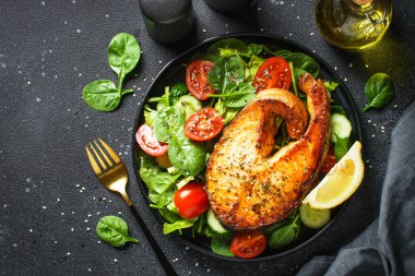 Somon bifteği ve siyah arka planda taze yeşil salata. Keto diyeti, sağlıklı yiyecekler. Üst görünüm kopyalama alanı.