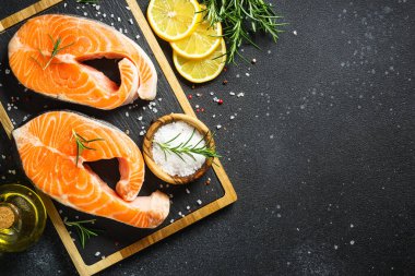 Siyah arka planda kesilmiş somon bifteği. Yemek pişirmek için malzemelerle üst görünüm.