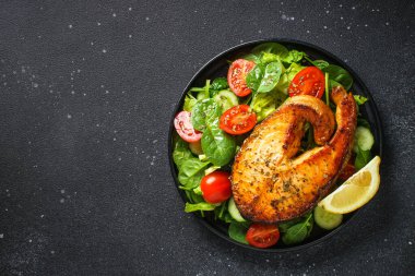 Siyah arka planda somon balığı ve yeşil salata. Fırında somon bifteği, Keto diyeti, sağlıklı yiyecekler. Kopyalama alanı olan üst görünüm.