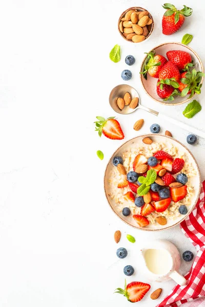 stock image Oatmeal porrige with fresh berries and nuts on white background. Healthy breakfast, top view with copy space.