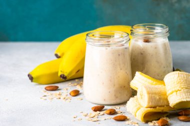 Almond banana smoothie with oat flakes in glass jars at white table.