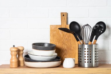 Kitchen table, kitchen utensils, plates, bowls, shakers and wooden cutting board, white modern interior. Modern kitchen interior.