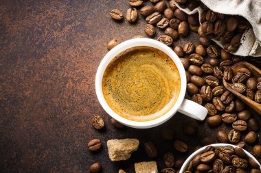 Cup of coffee, roasted coffee beans and sugar at dark table . Top view image with copy space.