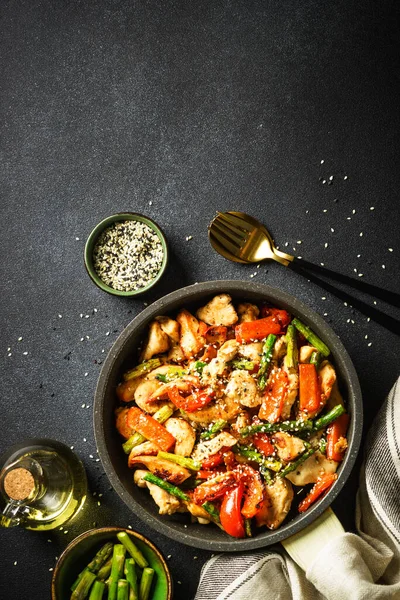 Chicken stir fry with vegetables in the skillet at black stone background. Top view with copy space.