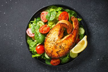 Siyah arka planda somon balığı ve yeşil salata. Fırında somon bifteği, Keto diyeti, sağlıklı yiyecekler. Kopyalama alanı olan üst görünüm.