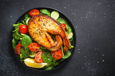 Somon bifteği ve siyah arka planda taze yeşil salata. Keto diyeti, sağlıklı yiyecekler. Üst görünüm kopyalama alanı.
