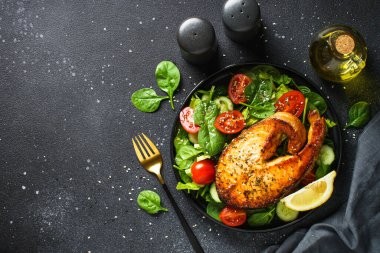 Somon bifteği ve siyah arka planda taze yeşil salata. Keto diyeti, sağlıklı yiyecekler. Üst görünüm kopyalama alanı.