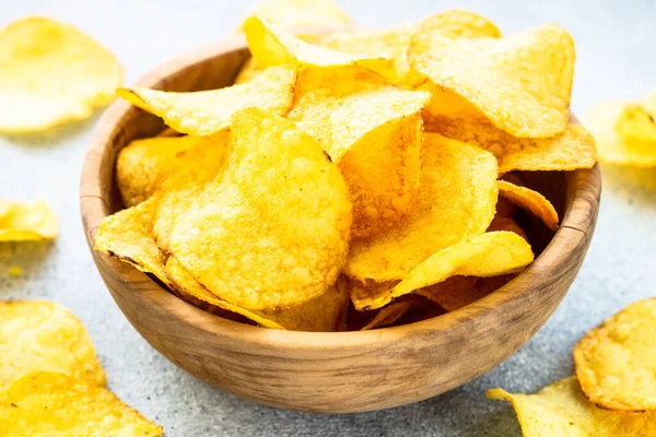 Potato chips in wooden bowl on white table. Top view with copy space.
