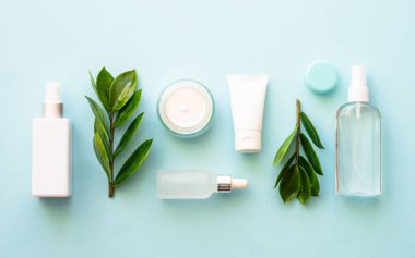 Doğal kozmetik ürünleri. Krema, serum, yeşil yapraklı tonik. Mavinin üzerinde düz uzanmış.