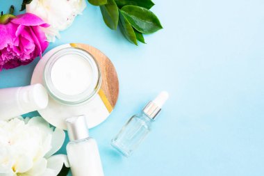 Doğal kozmetik ürünleri mavinin üzerine saçılmıştı. Krema, sabun ve yeşil yapraklı ve çiçekli serum şişesi..