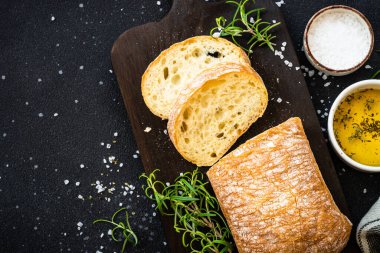 Tahtada ciabatta ekmeği, zeytinyağı, deniz tuzu ve siyah otlar. Kopyalama alanı olan üst görünüm.