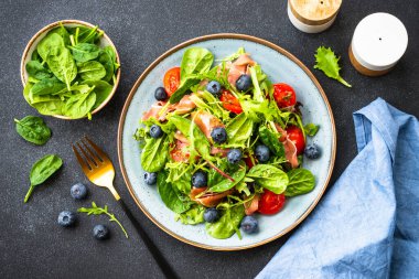 Taze jambonlu yeşil salata, yeşil yapraklar ve domatesler koyu masada. Kopyalama alanı olan üst görünüm.