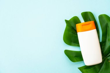 Mavi arka planda palmiye yapraklı güneş kremi ürünü. Metin için alanı olan düz resim.