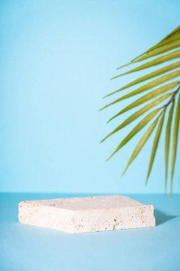 Stone podium for presentation cosmetic products on blue background with palm leaves.