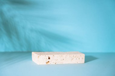 Mavi zemin üzerinde palmiye gölgeli kozmetik ürünlerinin sunumu için taş podyum.