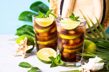 Küba Libre alkollü kokteyli, tropikal yapraklı buzlu içecek ve deniz kabukları. Yaz tatili.