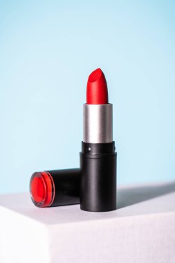 Mavi arka planda beyaz podyumda kırmızı ruj. Makyaj, kozmetik ürünler.
