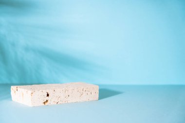 Travertine podyumu mavi arka planda kozmetik ürünler sunumu için. Palmiye yaprakları gölge.