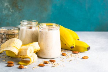 Almond banana smoothie with oat flakes in glass jars at white table.