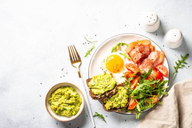 Healthy breakfast or lunch. Beacon, eggs, toast with avocado and fresh salad. Top view on white kitchen table.