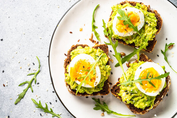 Open sandwich. Whole grain bread with avocado and boiled eggs. Top view on white kitchen table.