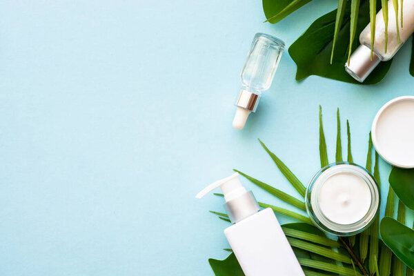Natural cosmetic products. Cream, serum, tonic with green tropical leaves. Flat lay on blue background with space for design.