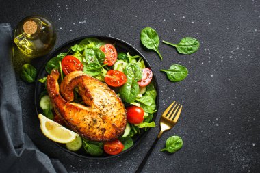 Somon bifteği ve siyah arka planda taze yeşil salata. Keto diyeti, sağlıklı yiyecekler. Üst görünüm kopyalama alanı.