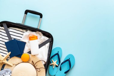 Yazlık kumaş, şapka, pasaport ve mavi arka planda parmak arası terliklerle dolu bavulu aç. İyi tatiller, seyahat konsepti. Düz görünüm.