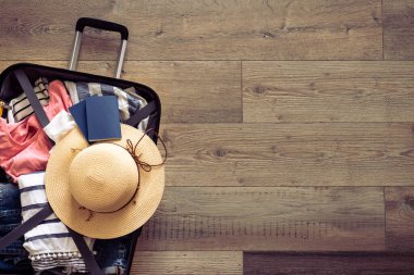 Seyahat geçmişi. Üzerinde yazlık kumaş, şapka ve tahta arka planda pasaportlar olan bavulu aç. Düz görüntü, geriye dönük ton.