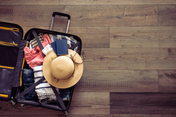 Travel background. Open Suitcase with summer cloth, hat, passports on wooden background. Flat lay image, retro toned.
