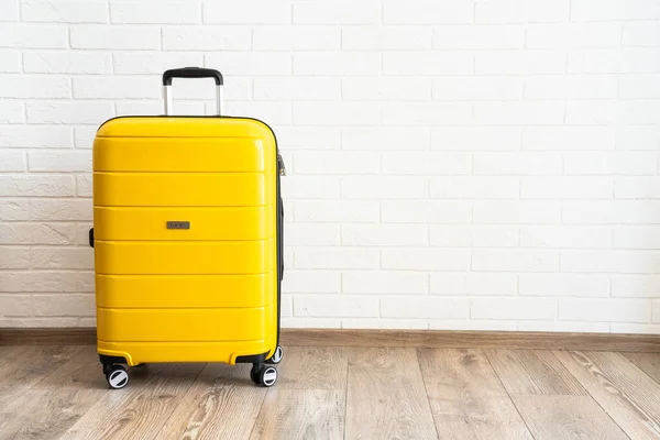 stock image Yellow baggage suitcase near white brick wall in the studio.