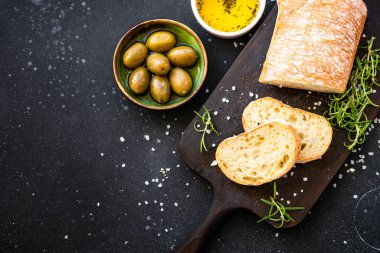 Tahtada ciabatta ekmeği, zeytin yağı, zeytin yağı ve siyah otlar. Kopyalama alanı olan üst görünüm.