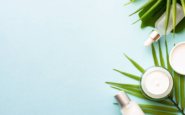 Summer cosmetic, set of cosmetic products with palm leaves on blue. Top view.