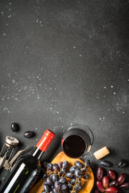 Kırmızı şarap siyah arka planda. Bir bardak şarap, şişe, çatal bıçak ve tirbuşon. Kopyalama alanı olan üst görünüm, dikey resim.