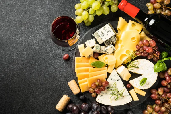 Cheese platter with craft cheese assortment, grape and red wine at black background. Top view with copy space.