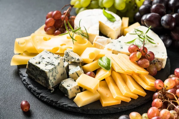 Cheese platter with craft cheese assortment and grape on slate board.