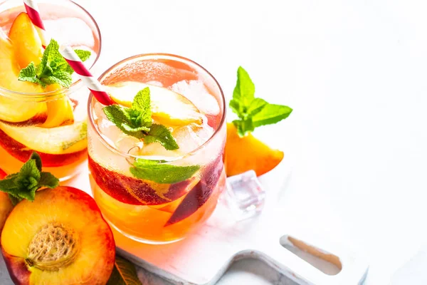 Peach tea, iced cold drink with fresh fruits, ice and mint. Close up with space for text.