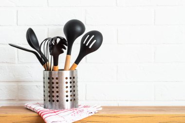 Kitchen utensils, cooking tools in black container near white wall.