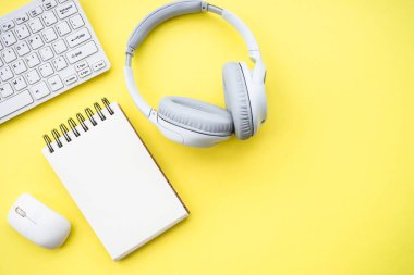 Office desk with headphones, notepad and pen at color background. Flat lay image with copy space.