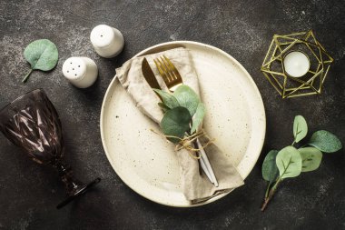 Table setting with white craft plate, cutlery and decorations at black stone table. Top view image.