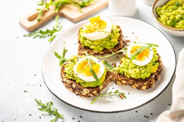 Open sandwich. Whole grain bread with avocado and boiled eggs. Top view on white kitchen table.