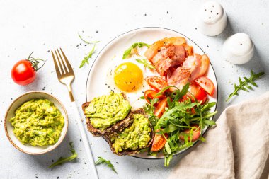Healthy breakfast or lunch. Beacon, eggs, toast with avocado and fresh salad. Top view on white kitchen table.