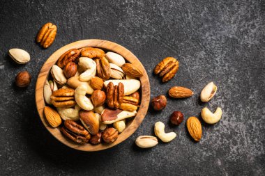Koyu taş masadaki ahşap kasede fındık çeşitleri. Kaju, fındık, badem, Brezilya fındığı ve ceviz. Kopyalama alanı olan üst görünüm.