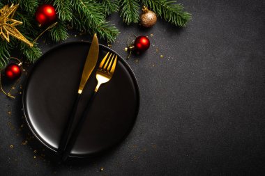 Siyah tabaklı Noel masası, altın çatal bıçak takımı ve tatil süslemeleri. Siyah üzerine üst görünüm.