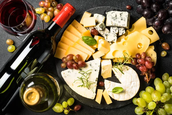 Cheese platter with craft cheese assortment, grape and wine at black background. Top view.