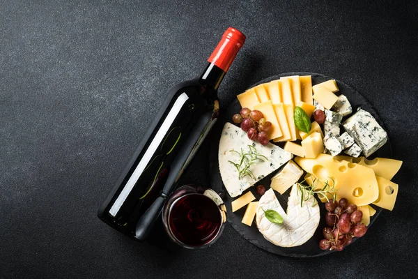 奶酪盘和红酒 切菜板上夹有新鲜葡萄的手工奶酪 黑色背景的顶视图 — 图库照片