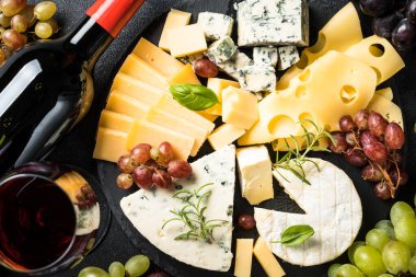 Tahta tahtada peynirli peynir tabağı ve siyah arka planda kırmızı şarap. Üst görünüm.