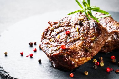 Et biftekleri. Siyah arka planda taş tahtada baharatlı ve otlu sığır eti madalyonları.
