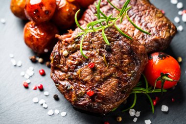 Barbekü yemeği. Siyah tahtada sebzeli et biftekleri ve otlar. Kapat..