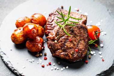 Barbekü yemeği. Siyah tahtada sebzeli et biftekleri ve otlar. Kapat..